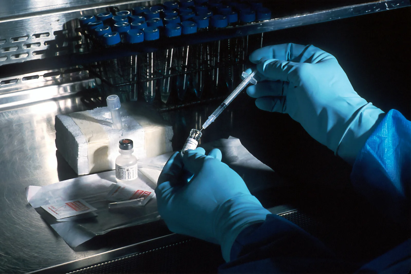 Mãos enluvadas preparando uma dose de medicamento biológico a partir de um frasco